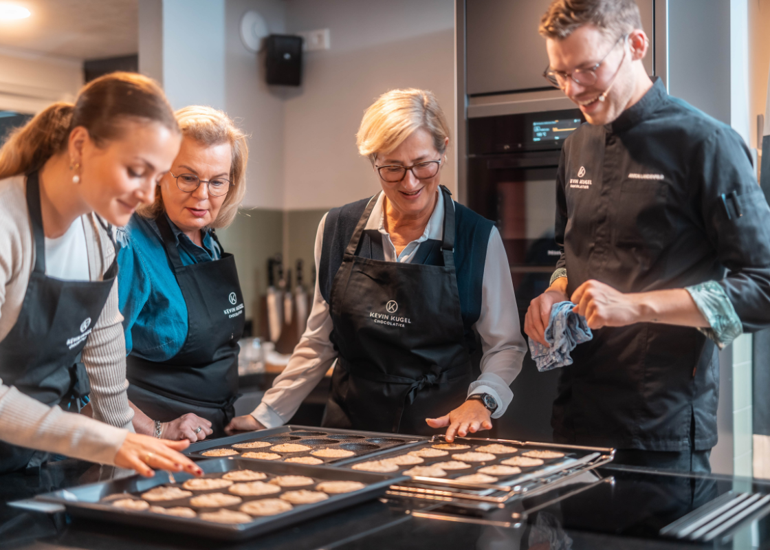 Der Chefpatissier steht mit Teilnehmern am Tisch, vor ihnen liegen zwei Bleche mit fertig gebackener Törtchenböden.